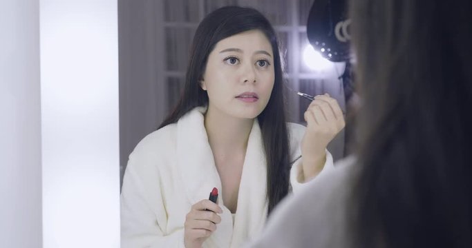 slow motion beautiful young asian japanese woman applying makeup in dressing room. elegant famous female model in makeup room backstage looking in mirror using brush to paint lipsticks on lips.