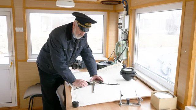 Planning a long trip on a cruise ship. Elderly grey-haired captain of the ship is plotting the navigation route on the map in the wheelhouse.
