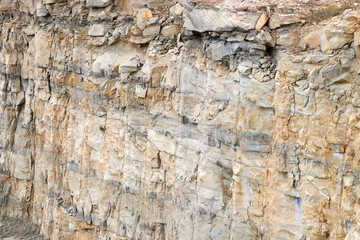 The rough-hewn vertical rock-face of a large working gravel quarry pit - a background of natural light-brown and grey colours - located near Ashby, NSW, Australia.