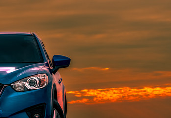Fototapeta na wymiar Front view of blue compact SUV car with sport and modern design parked on concrete road at sunset with beautiful orange sky. Electric car technology. Automotive industry. Car care business background.
