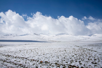 View of the snow-covered pasture and hills against the sky with clouds. Traveling in Kyrgyzstan