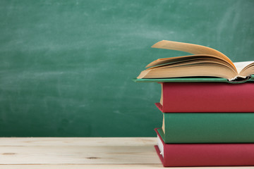 Education and reading concept - group of colorful books on the wooden table in the classroom, blackboard background
