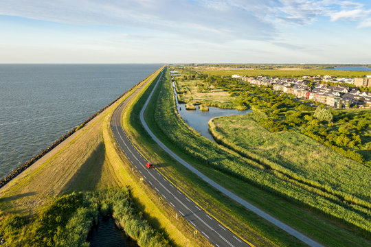 A dike in The Netherlands seen from the sky. A lake on the left, suburban area on the right.