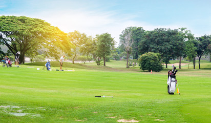 Golf bag with equipment on green grass in golf course on blurred golfers hit sweeping golf ball in...