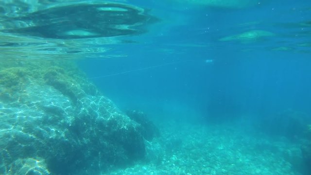 Rock underwater and move up to water surface to see boat anchored near rocky coast, Mediterranean sea, Spain, Costa Brava, Catalonia, Calella de Palafrugell