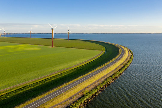 Wind turbines in a field in the Netherlands, next to a curved dike at a lake near Amsterdam.