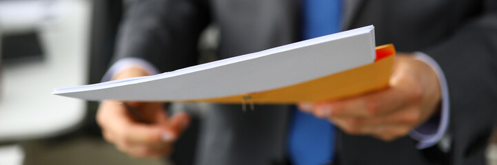 Clerk hand in suit and tie holding yellow envelope containing batch of important papers