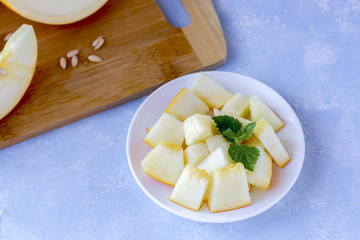 Ripe fresh yellow melon cut into pieces on a blue background.