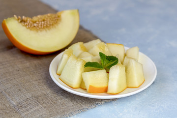 Ripe fresh yellow melon cut into pieces on a blue background.