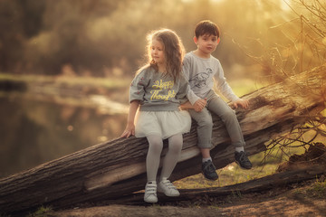 children sitting on the log in the spring park and holding hands