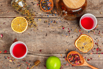 cups of healthy herbal tea with cinnamon, dried rose and camomile flowers in spoons over wooden...