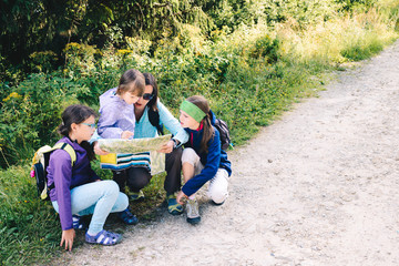 Family in the mountains during the climbing. Mom with daughters on a trip in the mountains. Studying the map - a mountain path in the background