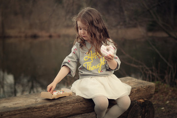 girl holding doughnut in the hand and taking another from the box sitting on the bench in the park