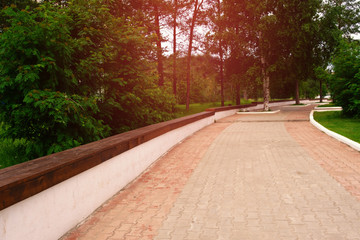 The road in the park with a long bench for relaxing on a sunny day.