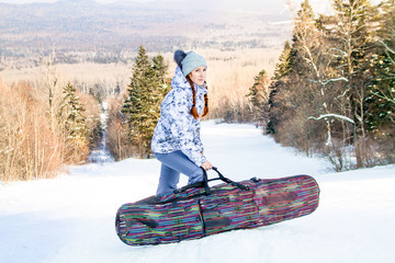 Girl snowboarder standing on a ski track, holding a case with her snowboard and enjoying the ski...