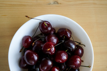 juicy ripe cherries with water drops in a white deep plate on a light wooden background