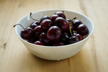 juicy ripe cherries with water drops in a white deep plate on a light wooden background