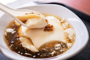 Popular Taiwan gourmet - Dessert of tapioca pearl ball (bubble) mixed bean curd tofu pudding (douhua, dou hua) in white bowl, close up, lifestyle