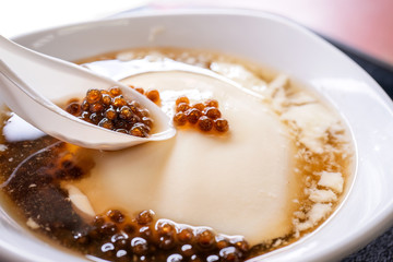 Popular Taiwan gourmet - Dessert of tapioca pearl ball (bubble) mixed bean curd tofu pudding (douhua, dou hua) in white bowl, close up, lifestyle