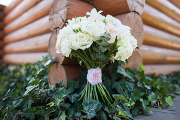 Wedding bouquet of white roses near the wooden wall of the log