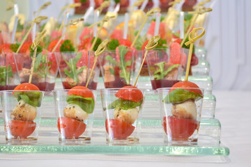 Different types of canapes in transparent glasses and wooden skewers on a glass step support on banquet