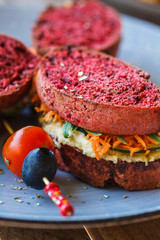 Vegan sandwiches for breakfast with beetroot bread, hummus and vegetables.
