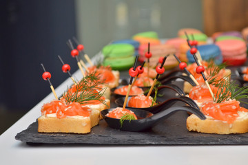 Canapes of bread and red fish, lie on a black stone board on the table at banquet, wooden and glass background