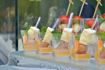 Differentmeet and cheese canapes in transparent glasses and wooden skewers on a glass step support on a banquet