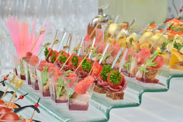 Different types of canapes in transparent glasses and wooden skewers on a glass step support on a banquet, side view
