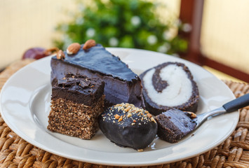 Various vegan desserts on a plate, outside in a cafe. Vegan cheesecake, candy, cake, coconut cake on white plate.