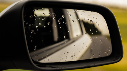 Abstract car window in raining day. View from car seat. Blur Background at sunset. Drops of rain on car window pane. Blurred droplet on car window, sun light over empty road. Driving in rain weather.