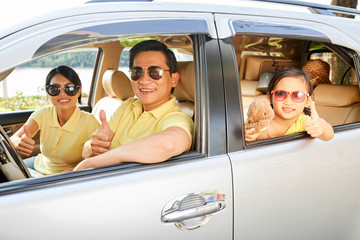 Portrait of Asian happy family in sunglasses sitting in their car showing thumbs up and they are going on summer holiday by car