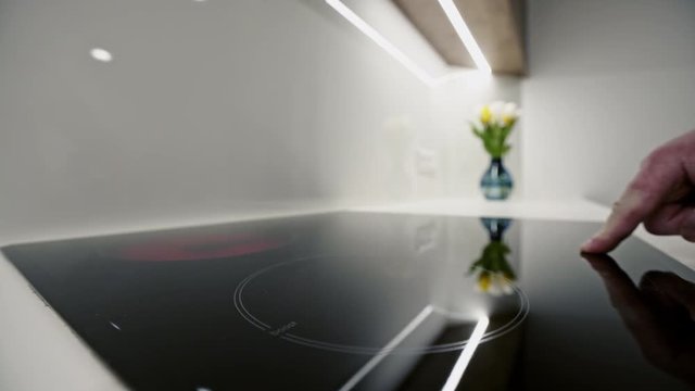 Hand of anonymous person pressing buttons on induction stove and changing burners temperature in stylish kitchen.