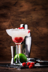 Raspberry daiquiri, alcoholic cocktail with white rum, lime juice, raspberries and crushed ice in tall glass, on wooden bar counter  with steel bar tools
