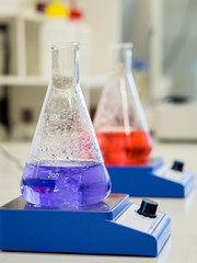 Erlenmeyer flasks with colorful solutions on a magnetic stirrer in a lab