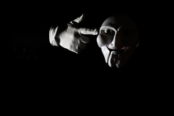 White scary mask on a black background with whites hand.