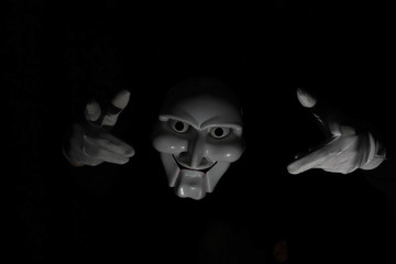 White scary mask on a black background with whites hand.