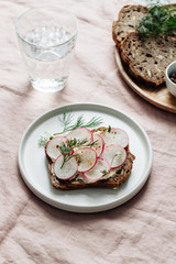 A slice of bread with bean paste, radishes and fresh dill on a table