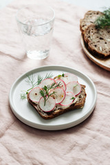 A slice of bread with bean paste, radishes and fresh dill on a table