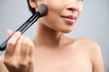 Close-up of young pretty woman applying blush on her cheek with make-up brush