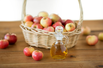 fruits, food and harvest concept - apples in wicker basket and glass jug of apple vinegar on wooden...