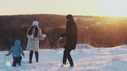 active family members in winter dressing play snowballs on snowy field against bright orange sunset slow motion