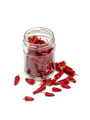 Hot red chili pepper in a glass jar and on a white surface