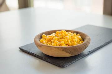 Wooden bowl with pile of yellow corn grains on stone slate, close-up