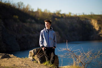 A young man stands at the rock of lake coast staring at the horizon. Confident in the future