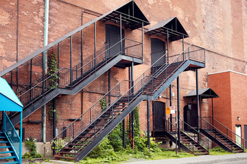 Old red brick industrial building facade with black iron outer ladder stairs.