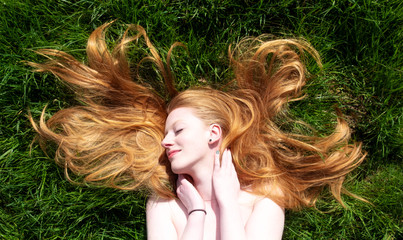 Portrait of a beautiful young sexy red-haired woman, lying in the spring sun relaxing on the green grass, the red hair draped freely around the head.