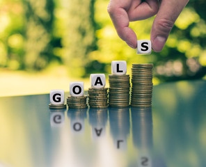 Concept of financial goals. Dice placed on increasing high stacks of coins form the word 