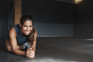 Attractive hispanic woman stretching body, sit with crossed leg, half-plank, doing fitness exercises, workout. Sportswoman warm-up before group training in gym, smile camera, motivated get fit
