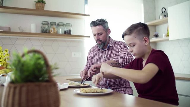 Mature father with small son indoors sitting at the table, eating pancakes.